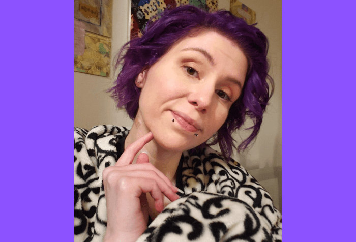 Graphic with a purple background featuring a photo of Kaalyn who is sitting looking to the camera with a light smile and forefinger to chin. She has purple chin-length hair, loosely curled, minimal makeup, and two black snakebite piercings at the lip. She's wrapped in a black and white decorative blanket in front of a wall of very colorful abstract art.