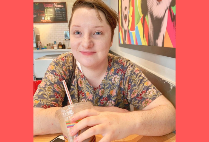 Graphic with a red background with a photo of Noah, a white trans masc non-binary person with short brown hair, smiles at the camera while holding a milkshake. They are wearing a short sleeved green shirt with red, orange, and pink flower pattern on it.