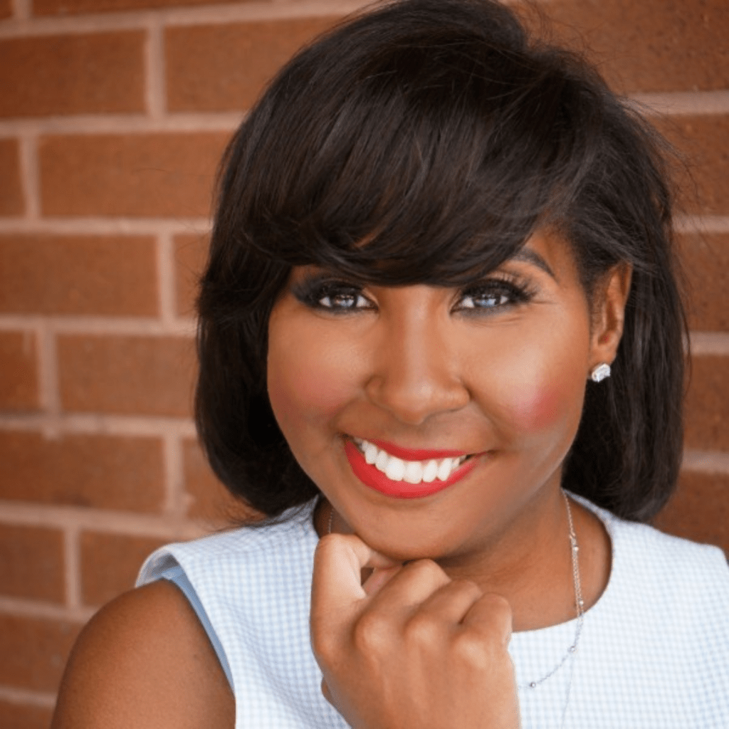Rasheera Dopson, MPH, a Black woman with medium-dark brown hair. She is wearing a sleeveless blue and white checkered top, with a silver necklace, wearing red lipstick and smiling.