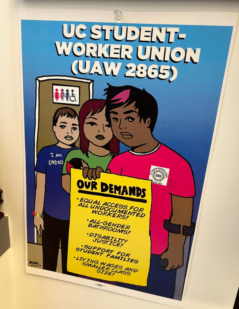 Colorful cartoon of three people standing in front of an all-gender restroom. One is wearing a UAW shirt, another’s shirt says “I am undocumented” and they are wearing a rainbow bracelet. Text at top of image reads “UC Student-Worker Union (UAW 2865).” The person with an arm brace at the front of the poster holds up a sign reading “Our demands: equal access for all undocumented workers! All-gender bathrooms!  Disability justice! Support for student families. Living wages and smaller class size!” Credit: artwork by Julio Salgado, 2014. For the 2014 round of UAW-UC contract bargaining. 