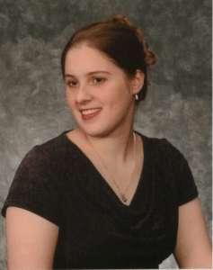 Image description: a young woman in a plum top with brown hair smiles and looks off to the side. 